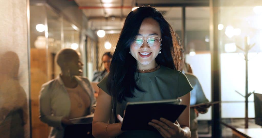 Night, tablet and business people walking in office after finishing work task. Tech, overtime and Asian woman with group of friends going home after working late on sales project in dark workplace