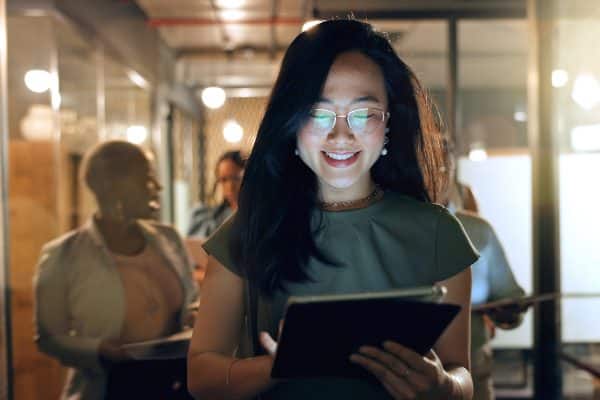 Night, tablet and business people walking in office after finishing work task. Tech, overtime and Asian woman with group of friends going home after working late on sales project in dark workplace
